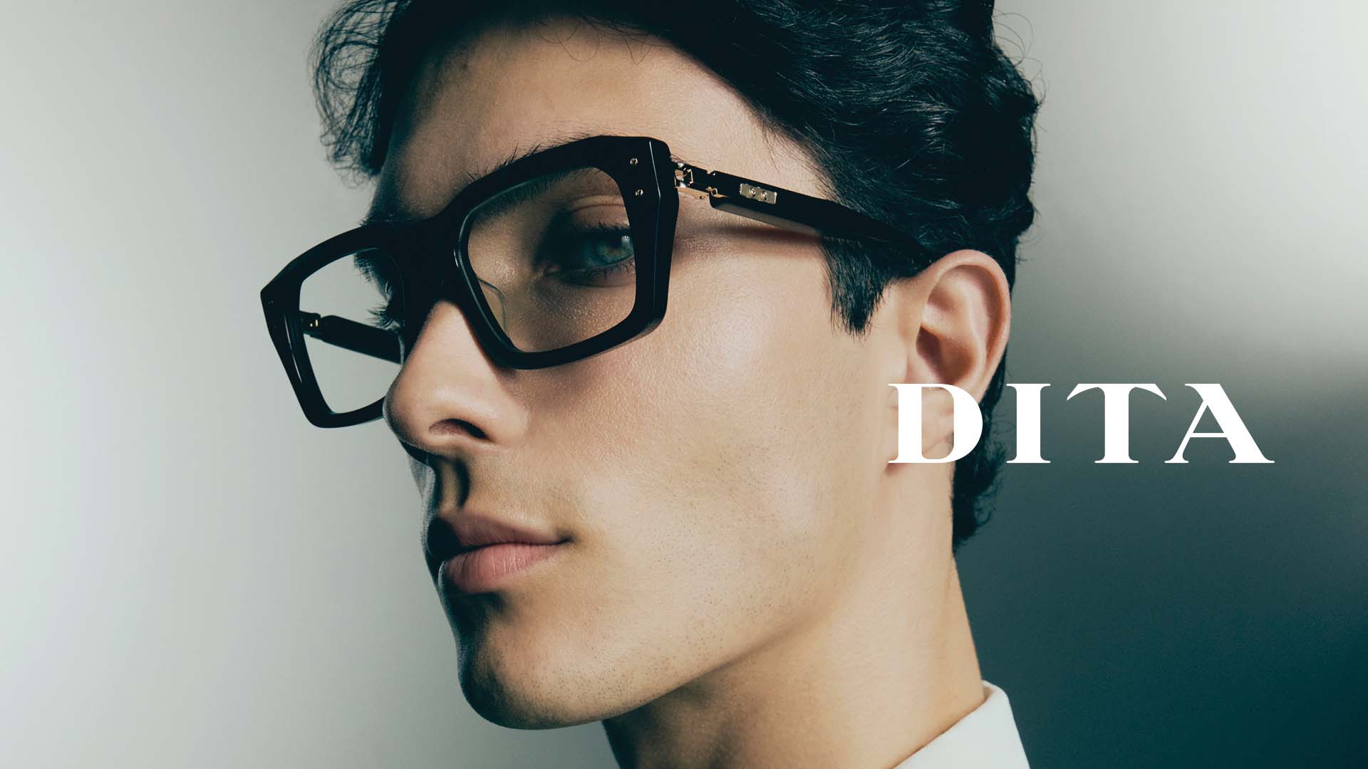 Plan rapproché d’un jeune homme, la tête légèrement inclinée, portant de grandes lunettes de soleil DITA rectangulaires avec des verres fumés qui souligne l’élégance urbaine des lunettes, désormais disponibles chez Winston Optique.