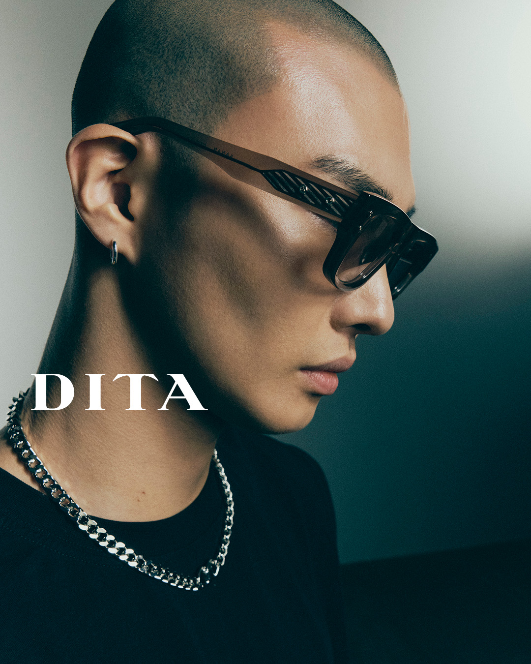 Plan rapproché d’un jeune homme, la tête légèrement inclinée, portant de grandes lunettes de soleil DITA rectangulaires avec des verres fumés qui souligne l’élégance urbaine des lunettes, désormais disponibles chez Winston Optique.